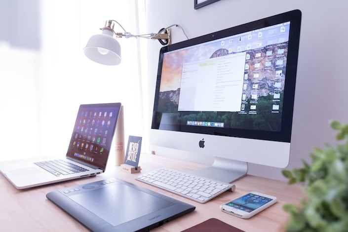 an apple brand desktop computer sitting on a desk with a laptop and a cellphone on either side of it