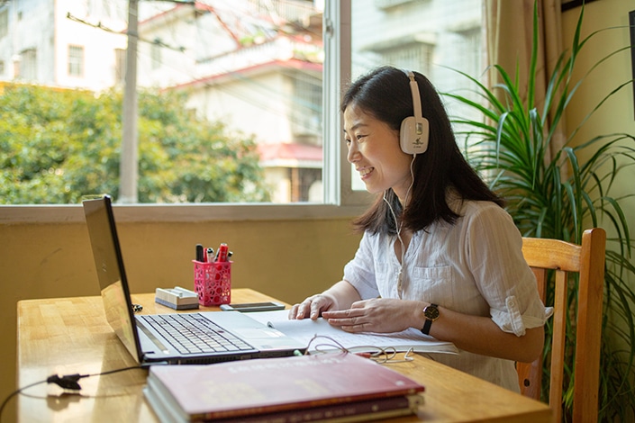 a CLI teacher sitting at a desk helping a student learn Chinese on Zoom