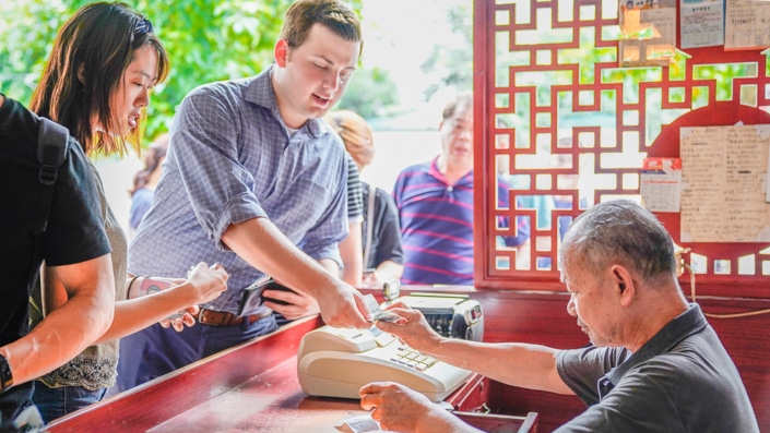 a Western man hands money to a Chinese shopkeeper