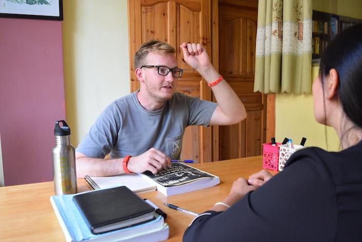 chinese language student with his fist at his forehead sitting at a wooden desk with chinese teacher
