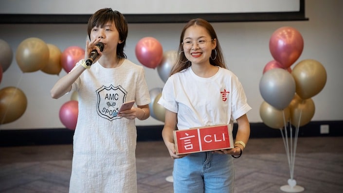 two CLI staff members stand with balloons in the background while hosting a raffle during a CLI anniversary event