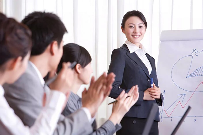 a Chinese career woman gives a presentation while colleagues look on