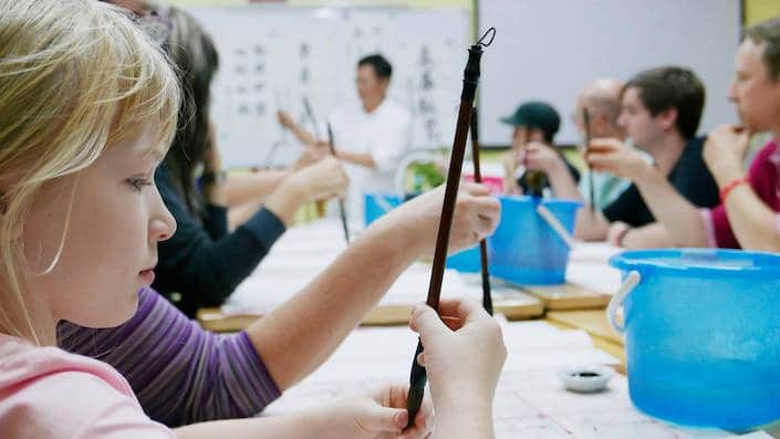 a blond girl holding a Chinese calligraphy brush