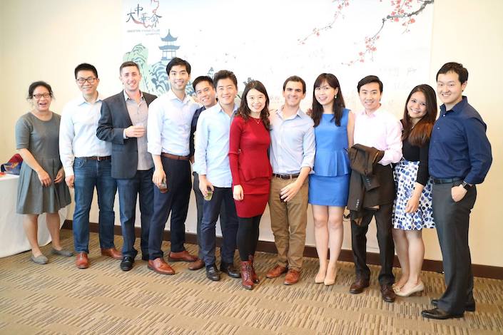 a group of men and women in business attire stand in a line against a wall with a traditional Chinese landscape painting on it
