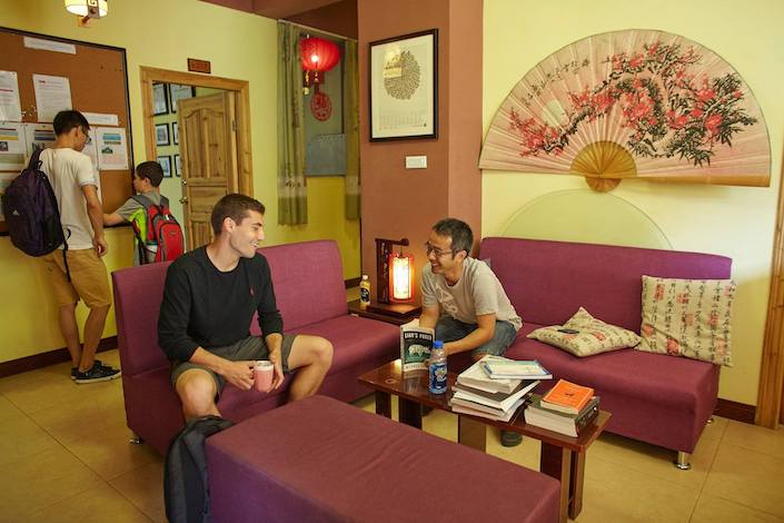 student chatting with local friend on purple couches with young boy and teaching facing a bulletin board in the background